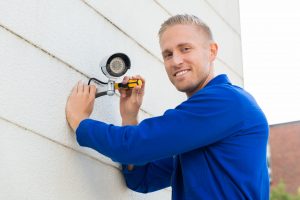 48038725 - smiling young technician installing camera on wall with screwdriver